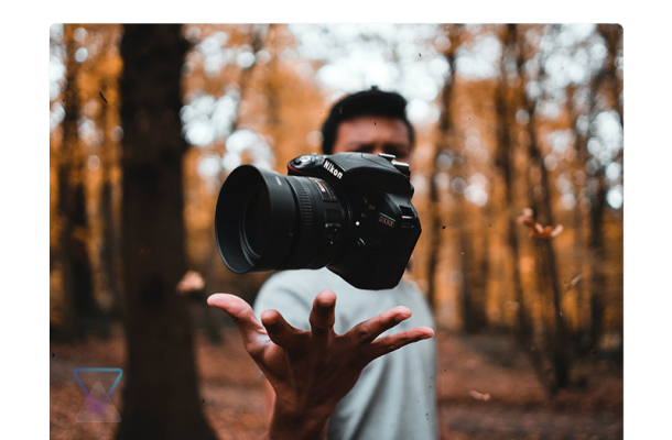 a man with golden aspens blurred in the background tossing a camera up above his hand