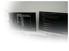 a desk with two monitors with html code on the one on the right and a website directory of files open on the left
