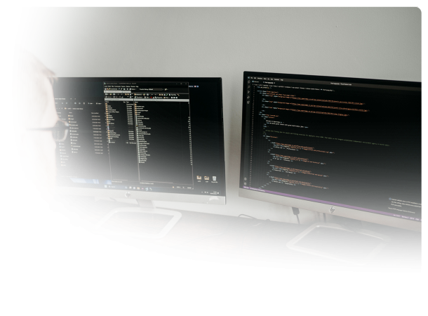 a desk with two monitors with html code on the one on the right and a website directory of files open on the left