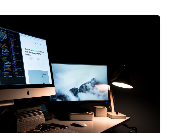 a macintosh with a second monitor with code on the left monitor and a cloudy mountain scene on the right monitor